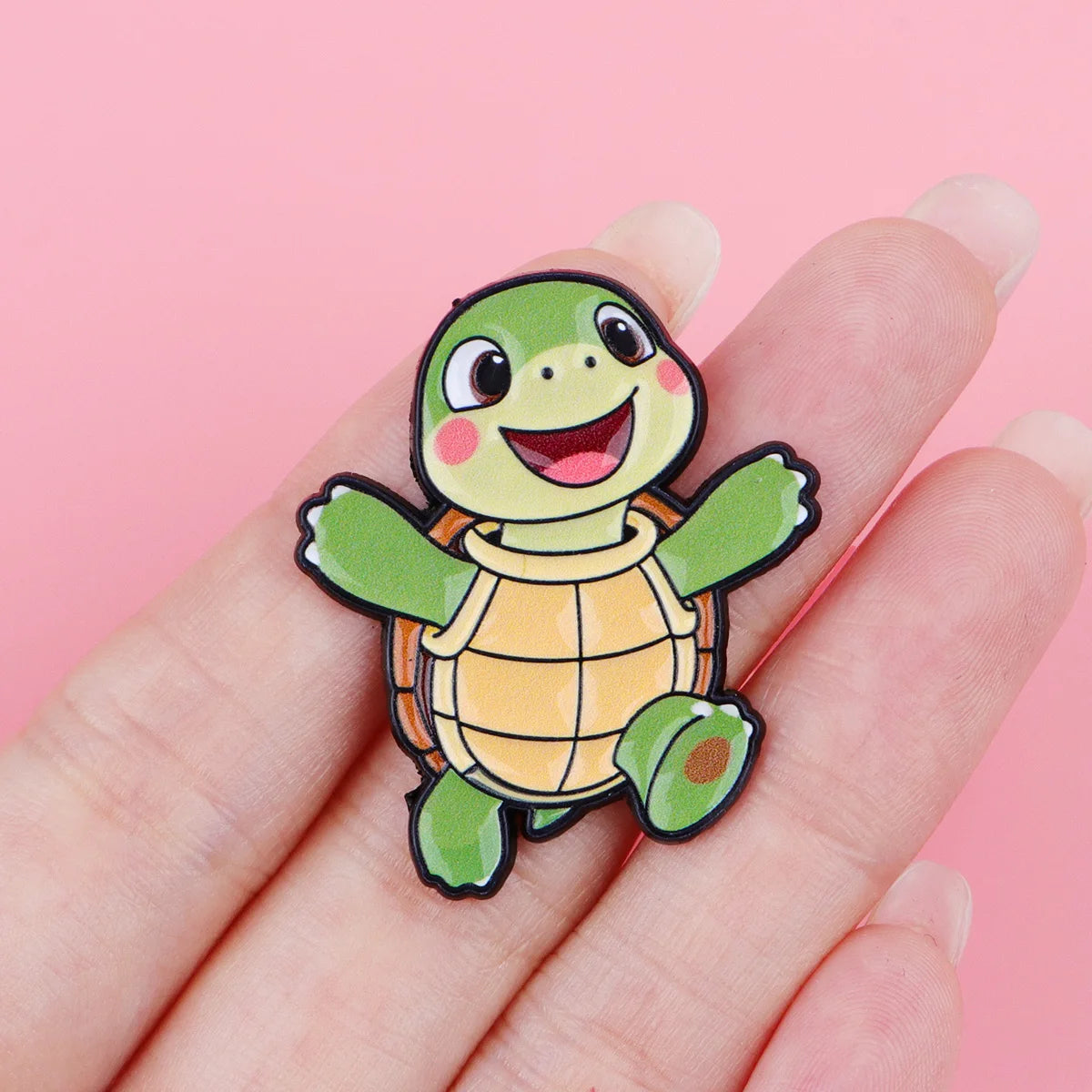 A hand holds a cute green turtle enamel pin featuring a smiling face and textured shell.