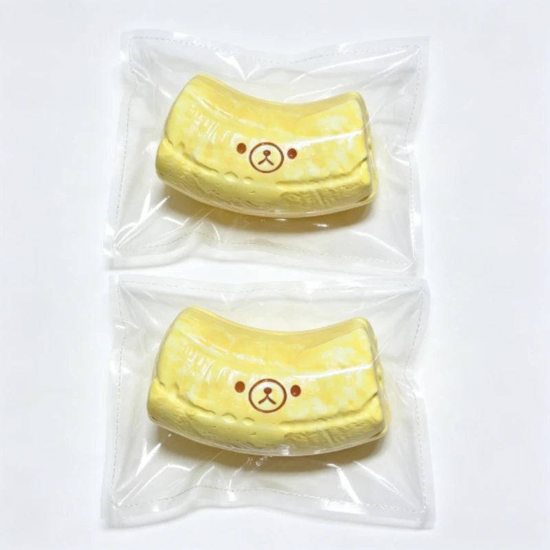 A yellow banana bear squishy stress relief toy with a butter-textured silicone finish, packaged in clear plastic.