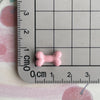 A small pink resin bone charm is placed on a ruler marked in centimeters and inches.