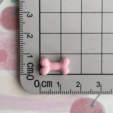 A small pink resin bone charm is placed on a ruler marked in centimeters and inches.