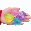 A hand holds four glowing, translucent squishy toys shaped like hearts in pink, yellow, purple, and blue.