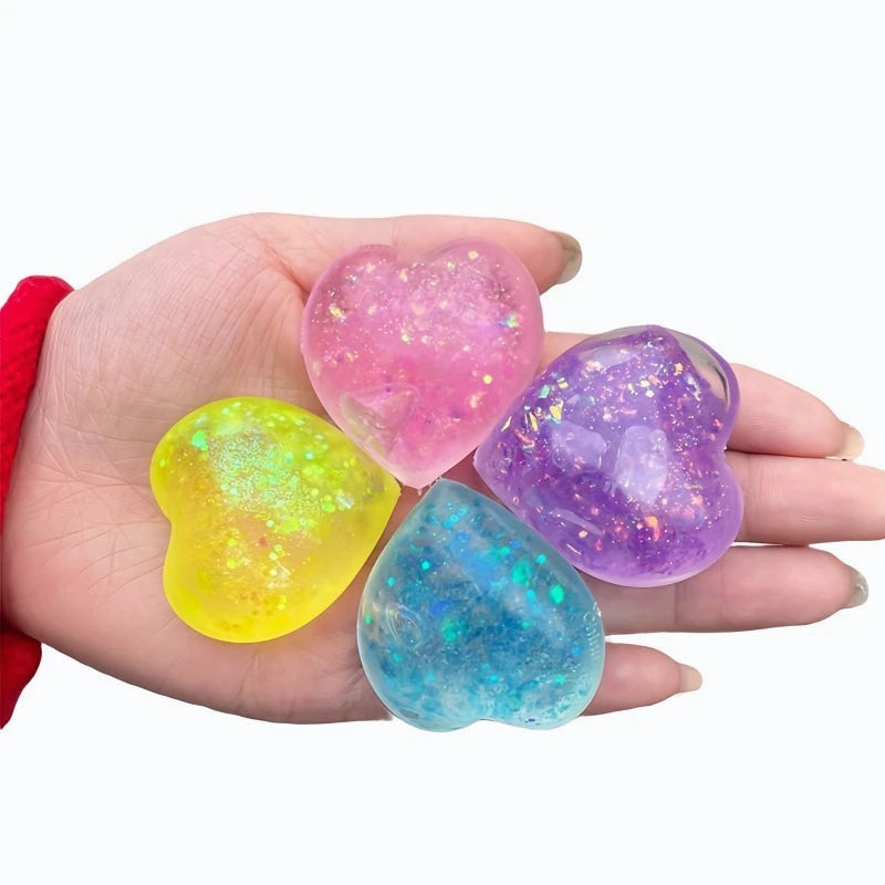 A hand holds four glowing, translucent squishy toys shaped like hearts in pink, yellow, purple, and blue.