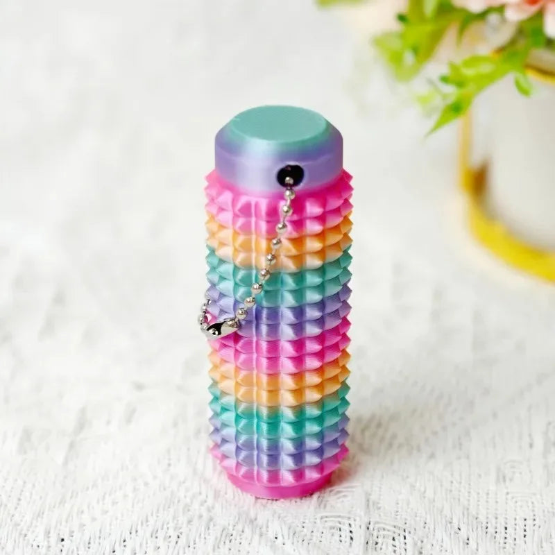 A colorful spiky sensory keychain with stacked layers of pastel colors sits on a white surface.