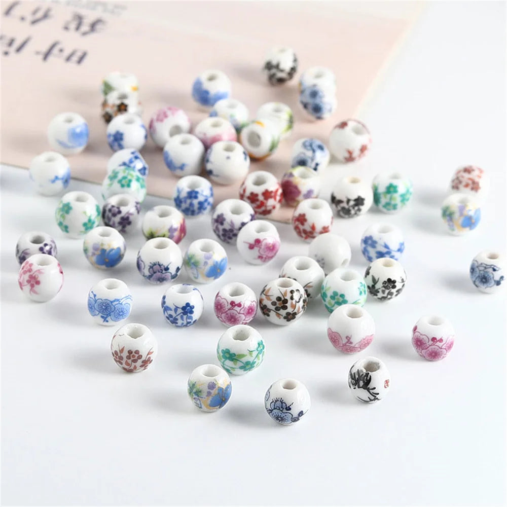A collection of round ceramic flower beads in various colors and patterns scattered on a white surface.