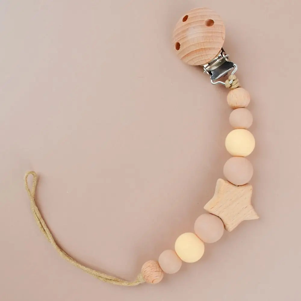 A wooden pacifier clip featuring silicone beads and a star shape on a light wood background.