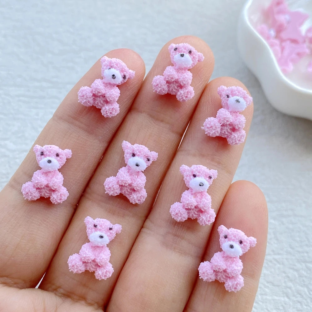 A hand displays several small pink resin teddy bear charms for DIY crafts.