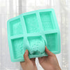 A hand holds a teal silicone soap mold with six cavities featuring lace patterns for crafting.