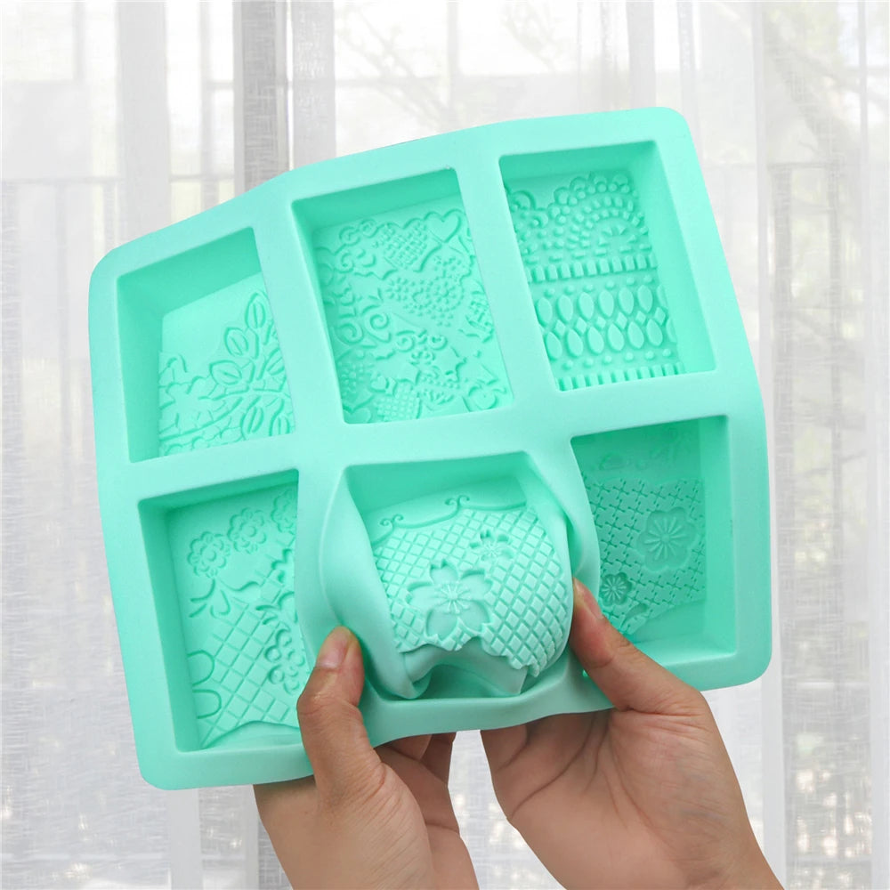 A hand holds a teal silicone soap mold with six cavities featuring lace patterns for crafting.
