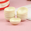 A set of ten small, white ceramic rice bowls stacked and displayed on a pink surface.