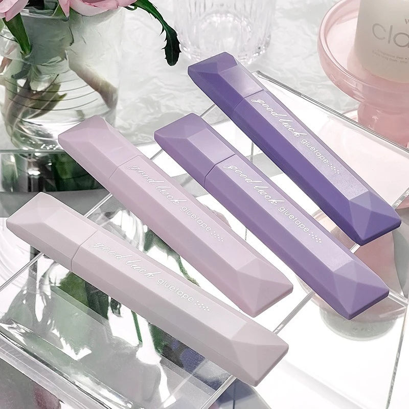 A collection of four purple and pink adhesive dot tape glue rollers displayed on a clear glass surface.