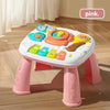 A pink musical baby piano playmat with a light-up keyboard and hanging toys is shown on a wooden floor.