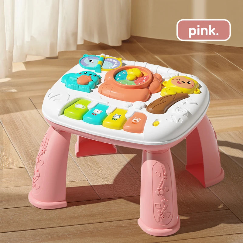 A pink musical baby piano playmat with a light-up keyboard and hanging toys is shown on a wooden floor.