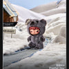 A small, gray plush doll with pink features is placed in a snowy landscape.