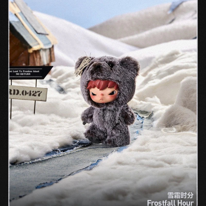 A small, gray plush doll with pink features is placed in a snowy landscape.