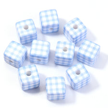 A collection of light blue and white plaid acrylic cube beads scattered on a white surface.