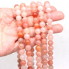 A hand holds multiple strands of round rose quartz beads in various shades of pink and orange.