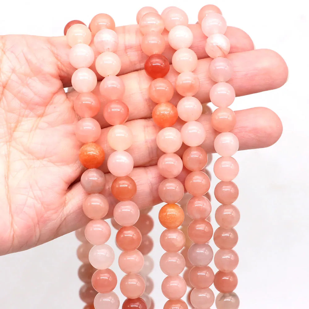 A hand holds multiple strands of round rose quartz beads in various shades of pink and orange.