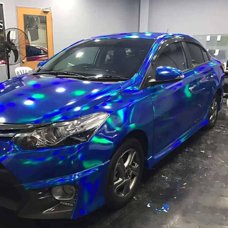A blue sedan wrapped in holographic chrome vinyl film, showing iridescent colors under the light.