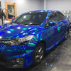 A blue sedan wrapped in holographic chrome vinyl film, showing iridescent colors under the light.