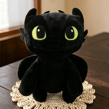 A black dragon plush toy with bright green eyes sitting on a woven mat.
