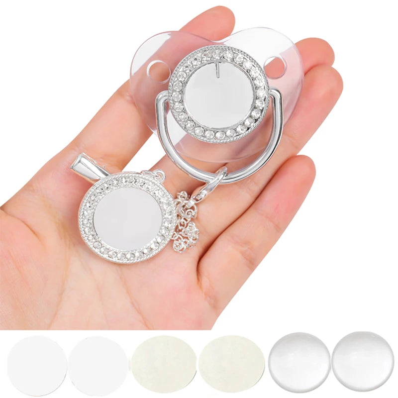A hand holds a clear silicone baby pacifier and clip set decorated with sparkling rhinestones.
