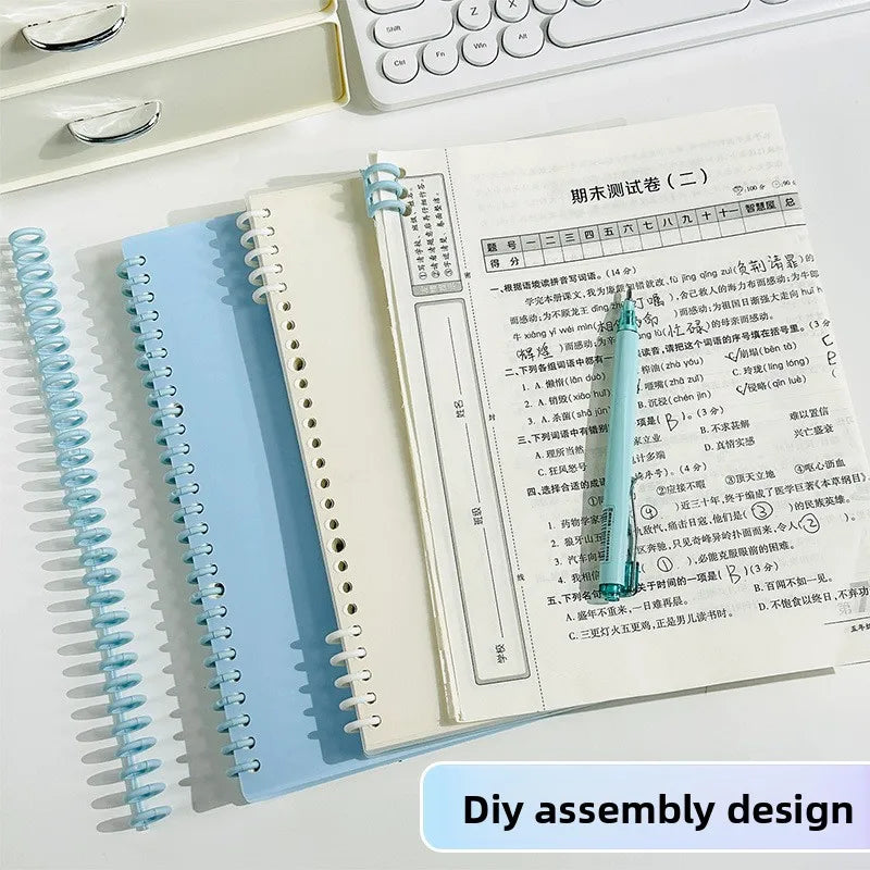 A spiral notebook with blue and white pages is shown next to a white keyboard and a pencil.