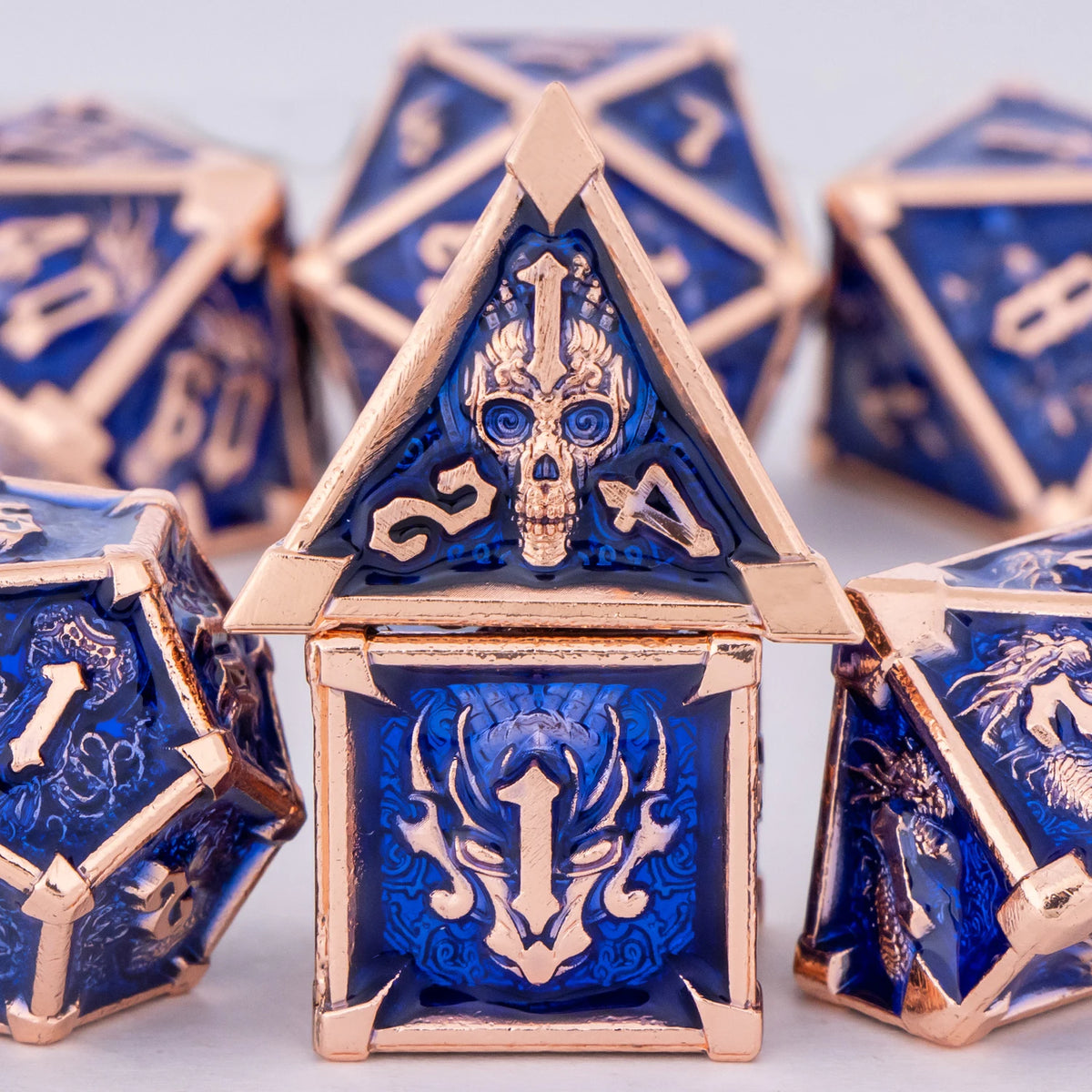 A close-up of a gold metal dice set featuring skull and dragon designs on blue dice.