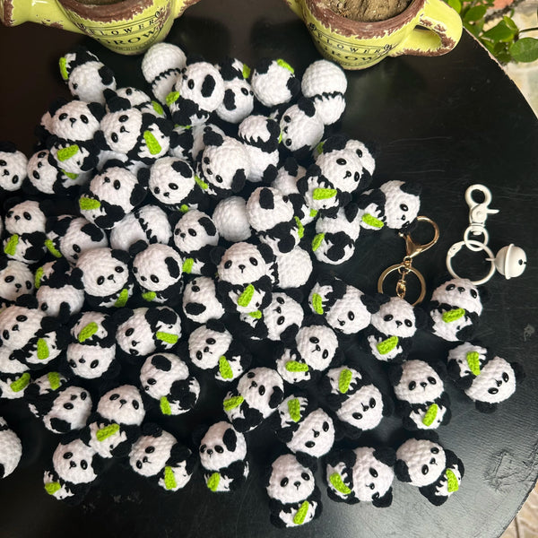 A collection of black and white crochet kitten keyrings with panda charms arranged on a dark surface.