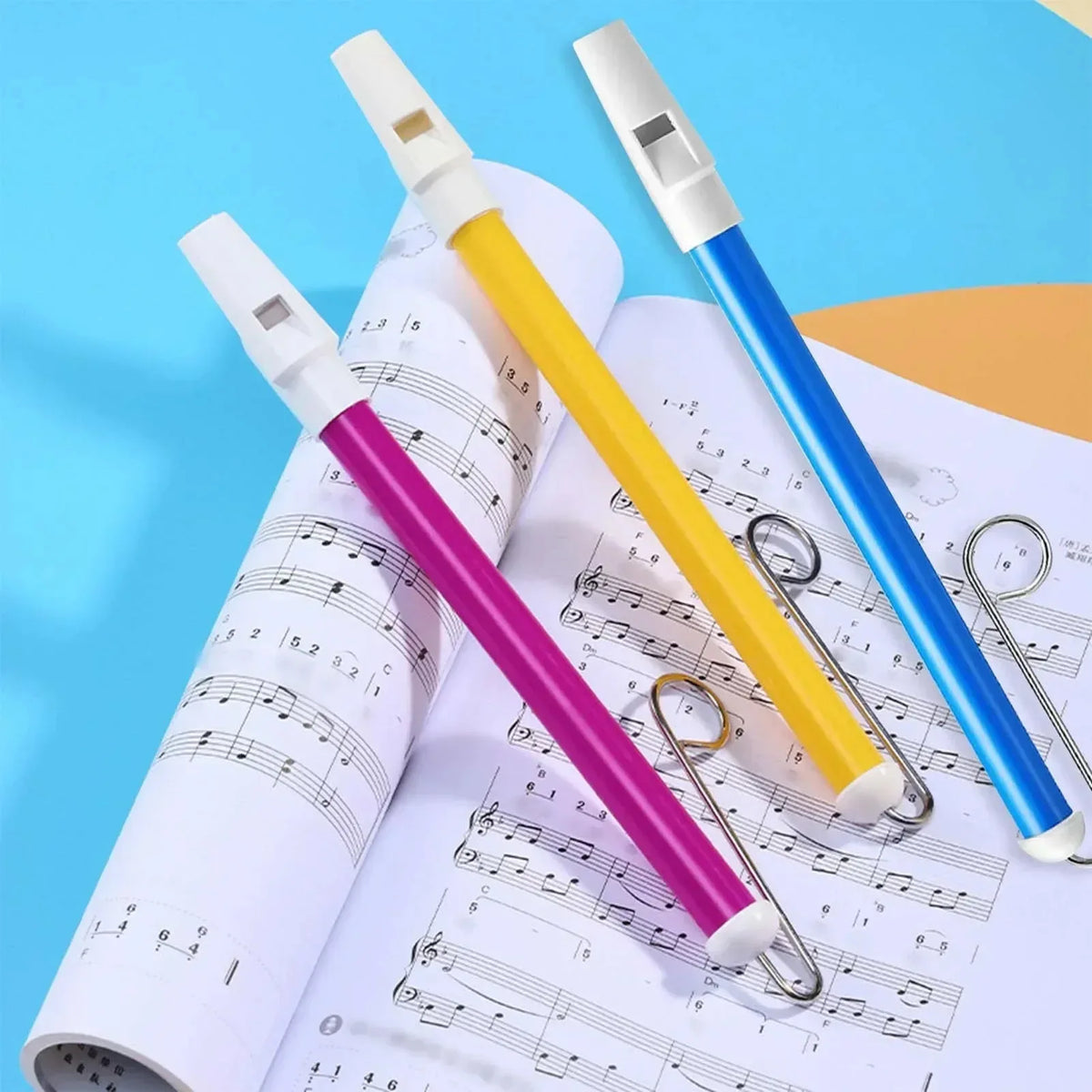 Three slide whistles in white, yellow, and blue are displayed on sheet music.