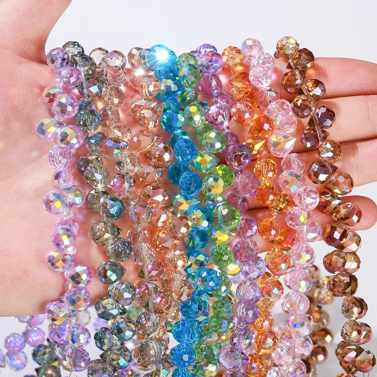 Eine Hand hält mehrere Stränge bunter facettierter Glasperlen in Violett-, Blau-, Pink- und Bernstein-Tönen.