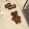 A beige cotton shirt features a brown embroidered text 'yuan chuang!' and a small brown bear patch on the chest.