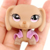 A small, light brown miniature pet animal figure with large eyes and a purple accessory is held in a hand.