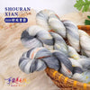 A bundle of hand-dyed Australian wool yarn in a gradient of gray and white is shown in a woven basket.
