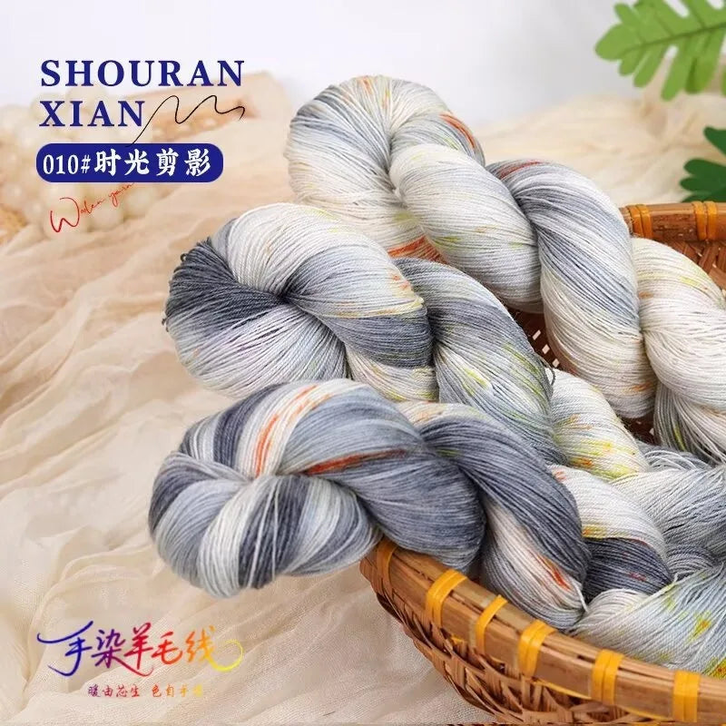 A bundle of hand-dyed Australian wool yarn in a gradient of gray and white is shown in a woven basket.