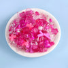 A pile of pink and magenta acrylic beads for DIY jewelry making is displayed in a white bowl.