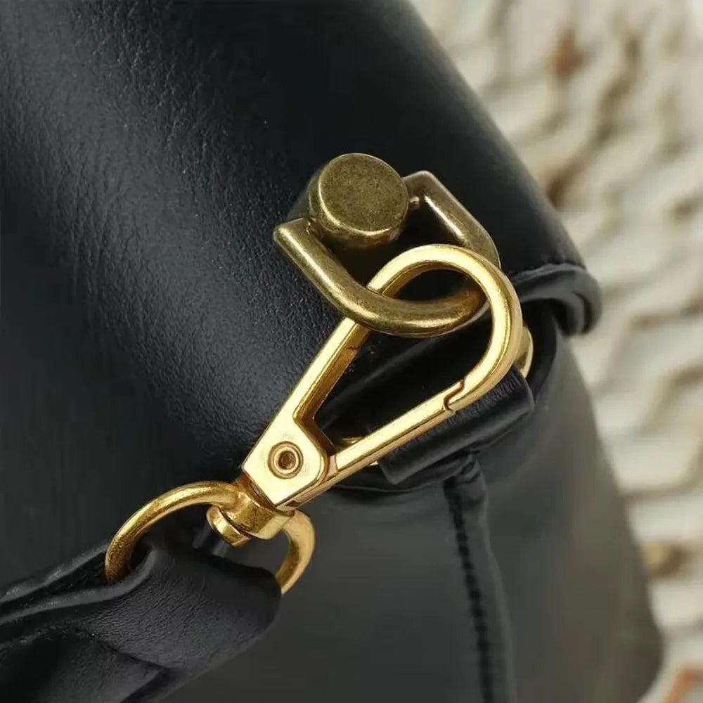 Close-up of gold D-shaped metal bag handles attached to a black leather strap on a purse.