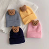 A collection of three knitted baby hats in gray, yellow, and pink, each featuring a small brown bear ear.