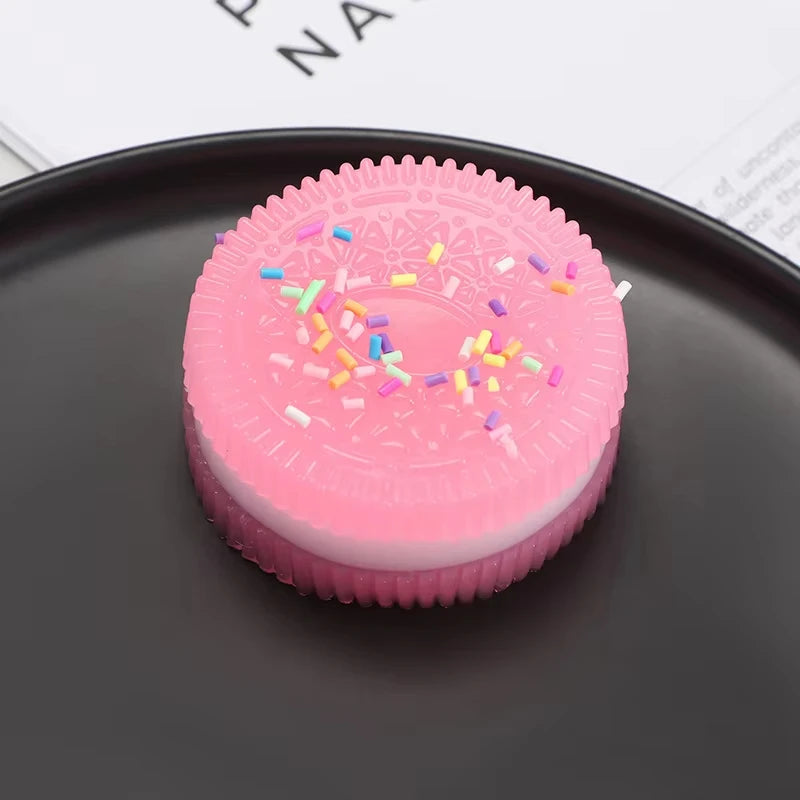A pink biscuit squishy stress relief toy with colorful sprinkles resting on a dark plate.