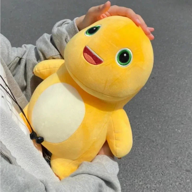 A yellow dinosaur plush toy with large eyes and a white belly is being held in a person's hand.