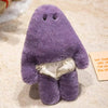 A purple monster plush doll with a slightly elongated body and fabric pants is shown resting on a light-colored surface.
