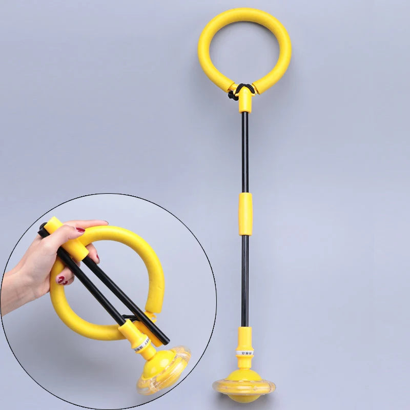 A yellow twist and jump ball with a tether is shown being held by a hand against a light gray background.