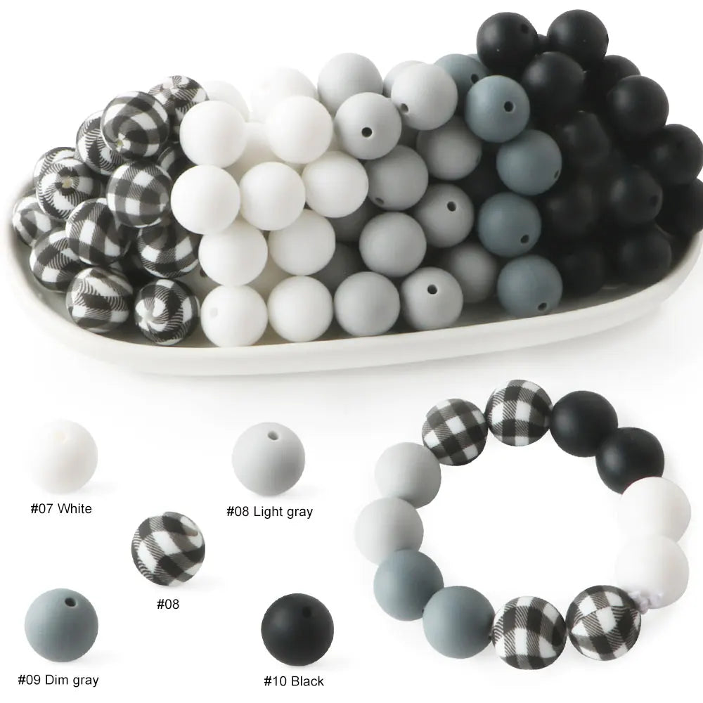 A collection of soft food-grade silicone beads in various shades of white, gray, and black arranged on a white plate.