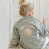 A young child is shown from the back wearing a light green padded jacket with a moon design print.