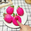 A hand is squeezing a bright pink dragon fruit squishy stress relief toy on a white plate.