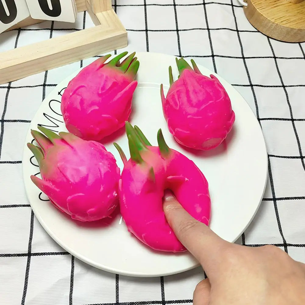 A hand is squeezing a bright pink dragon fruit squishy stress relief toy on a white plate.