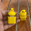 A yellow duck fidget clicker keychain with a frog design is held in a hand against a wooden background.