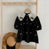 Black girls party dress with white lace collar and embroidered bows hanging on a wooden rack.