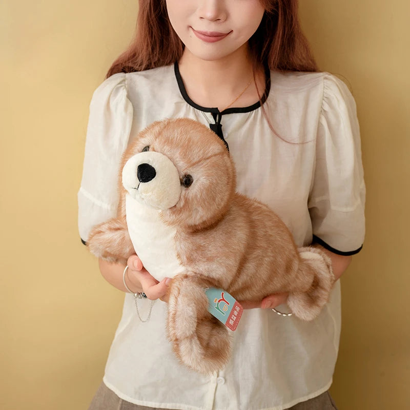 A woman holds a brown seal plush toy against her white shirt.