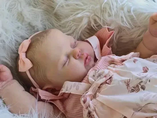 A newborn baby doll with hand-painted skin is sleeping peacefully on a white, fluffy surface.