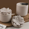 A white floral silicone mold for decorative storage jars and candle cups sits on a cork coaster.